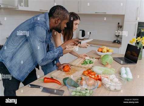 A Married Couple Cooks Together Using A Laptop Searching For Recipes On The Internet An