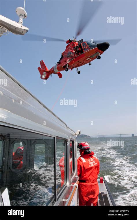 A United States Coast Guard Hh 65C Dolphin Helicopter Lowers A Rescue Basket To The Deck Of A